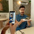 Excited man holds plate in restaurant while woman takes a photo.png