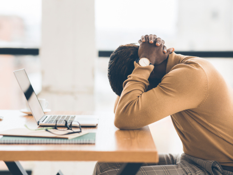 Exhausted African man with his head on his table and hands at the back of his neck