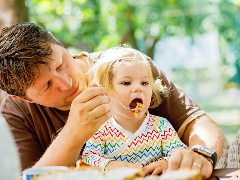 Father feeding cute little toddler girl in restaurant