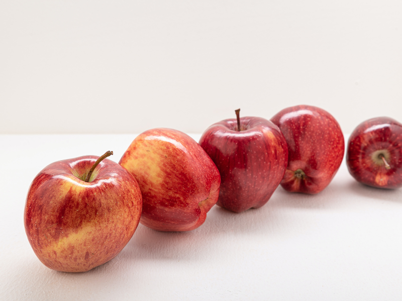 Five red apples on a white surface