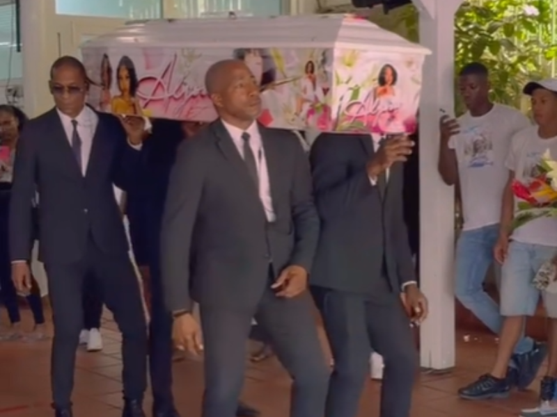 Four pallbearers dance while they hold up the casket at a funeral