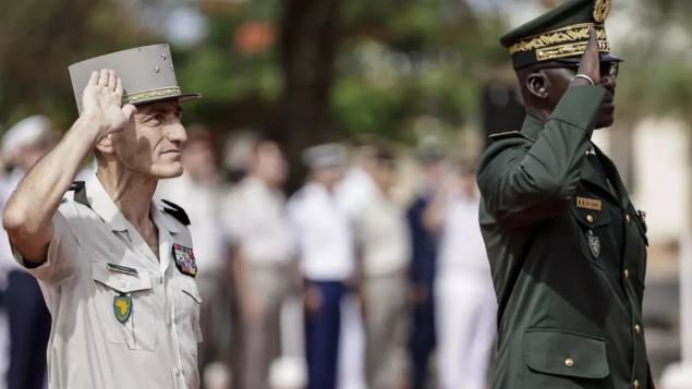 Generals Mbaye Cisse and Pascal Ianni salute as the Senegalese flag is raised
