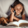Girl lying in the bed with her dog under blanket reading book