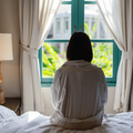 Girl sitting on a bed looking out a window