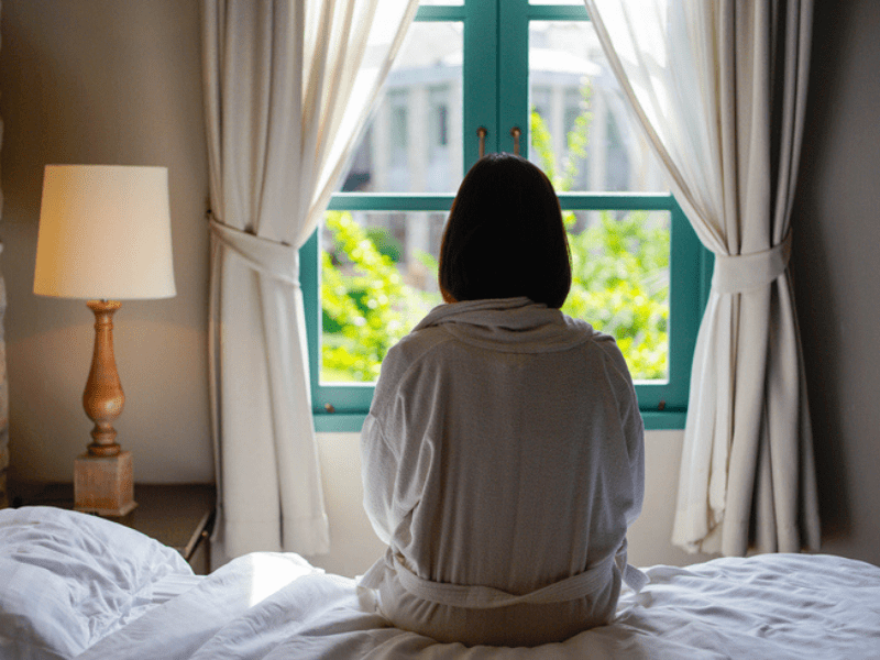 Girl sitting on a bed looking out a window
