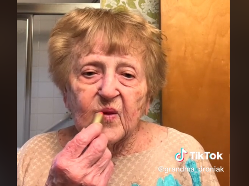 Grandmother applies lipstick in front of the mirror