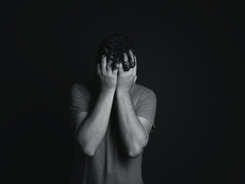 Gray scale photo of man covering face with his hands
