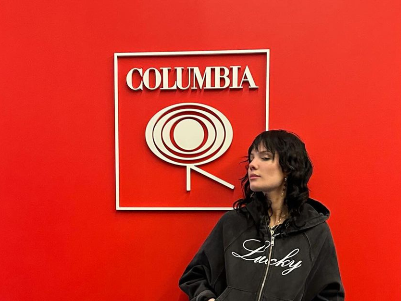 Halsey posing against a red wall with a Columbia logo