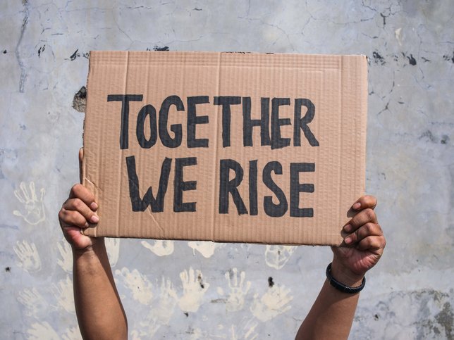 Hands holding protest signs with words Together We Rise
