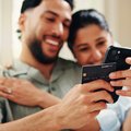 Happy couple holding credit card and making a  payment with phone in their home