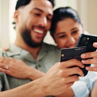 Happy couple holding credit card and making a  payment with phone in their home