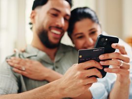 Happy couple holding credit card and making a  payment with phone in their home