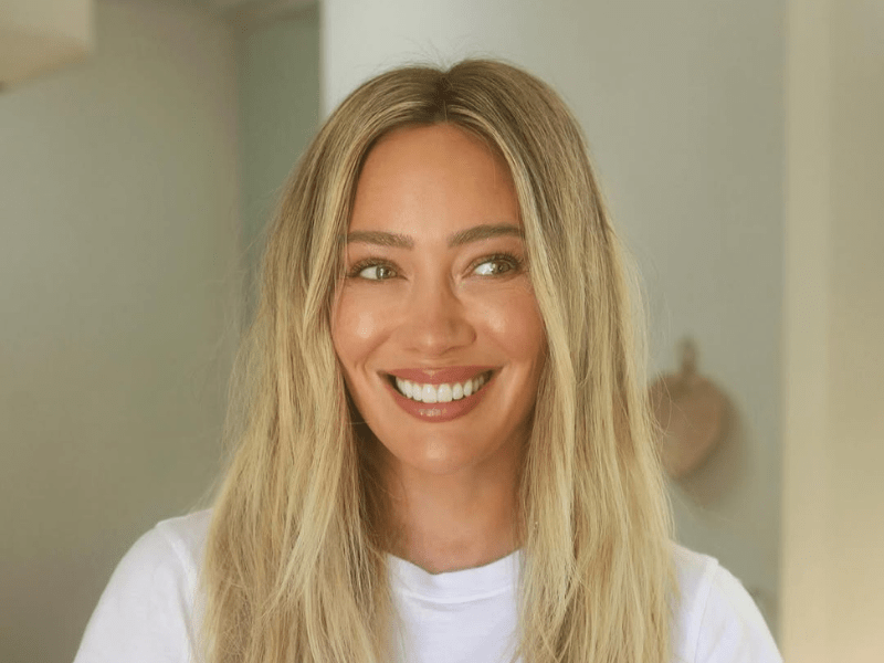 Hilary Duff smiles warmly while wearing a white t shirt