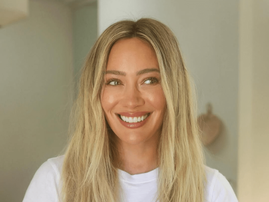 Hilary Duff smiles warmly while wearing a white t shirt