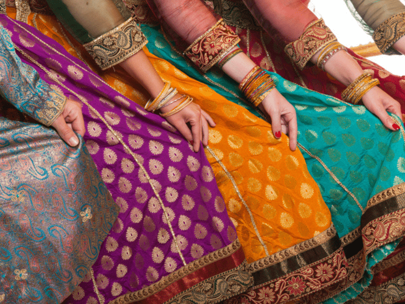 Indian women wearing bangles hold their traditional dresses with their hands