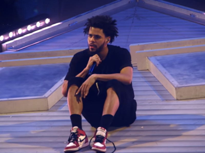 J. Cole sitting on a roof during a concert.png