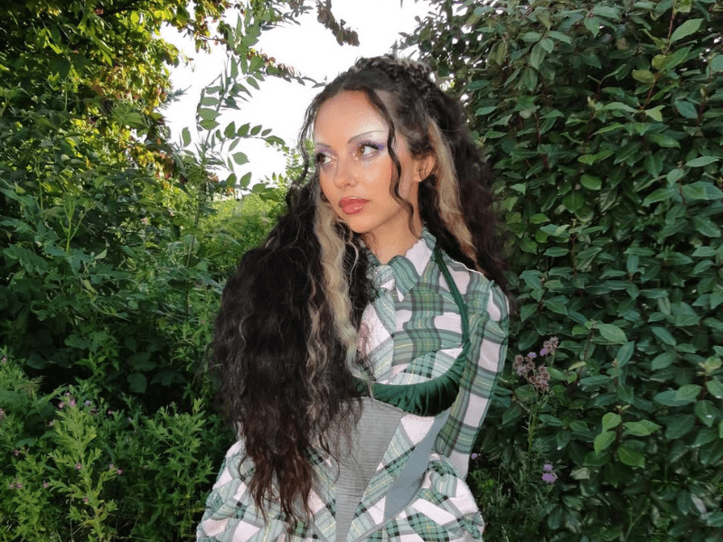 Jade Thirlwall poses next to a leafy green bush