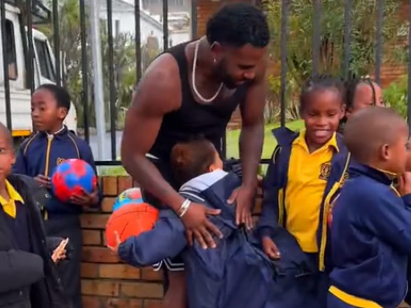 Jason Derulo hugs a child standing with a group of school kids