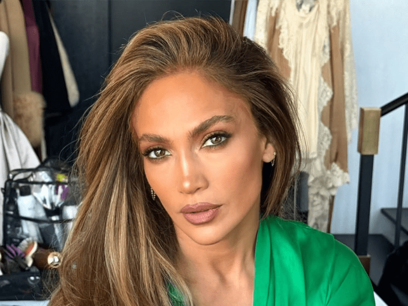 Jennifer Lopez wearing a green silk gown while sitting in a make up chair