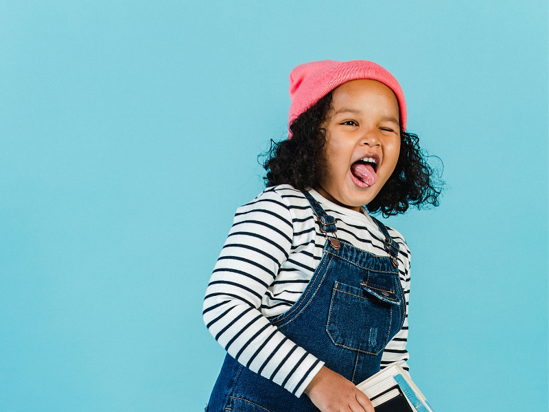 Joyful mixed-race girl with book grimacing in studio
