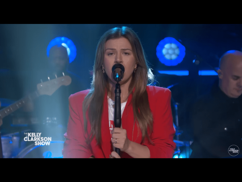 Kell Clarkson wears a red jacket while singing onstage