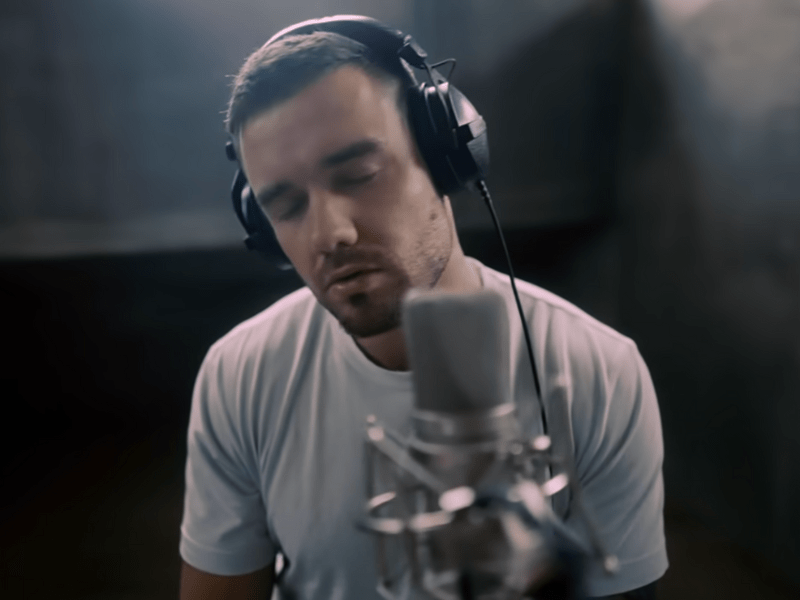 Liam Payne wearing large headphones while singing into a studio mic