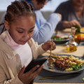 Little black girl watching the phone while eating dinner