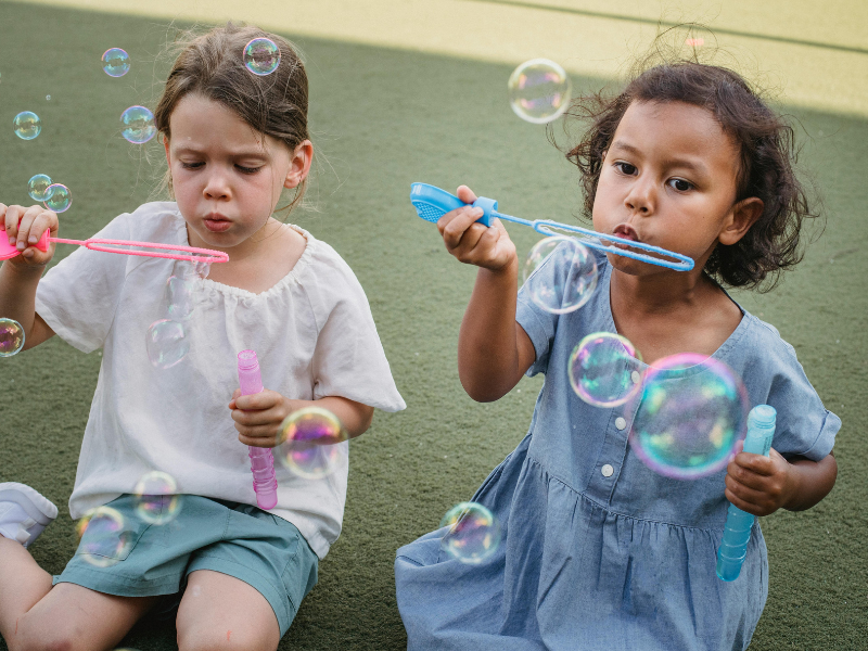 Little girls sitting on the ground blowing bubbles