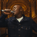 Lloyiso wears a dark denim blue jacket while singing in a cathedral