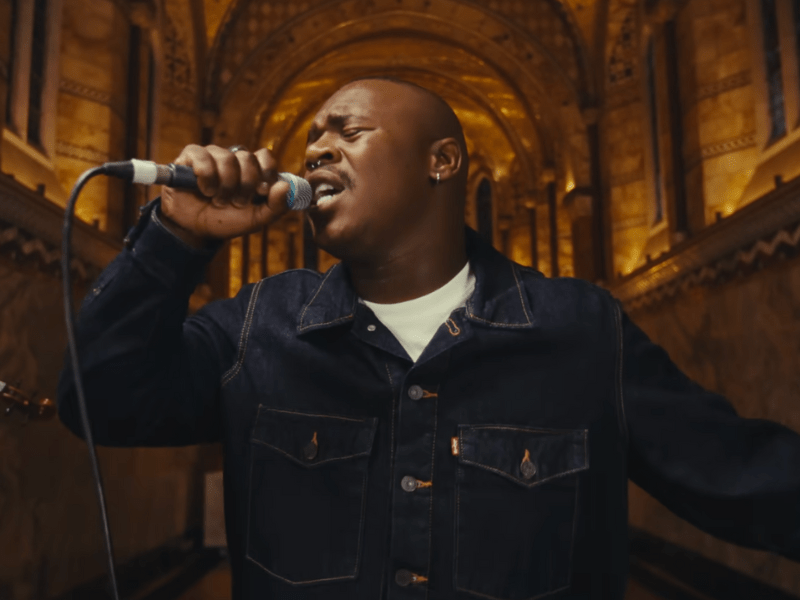 Lloyiso wears a dark denim blue jacket while singing in a cathedral
