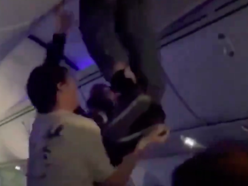 MAN IN OVERHEAD COMPARTMENT OF PLANE