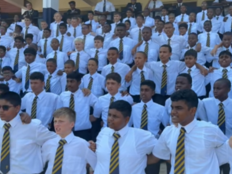 Male scholars join arms and perform their school war cry