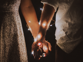 Man and woman holding each others hands wrapped with fairy lights