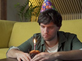 man celebrates his birthday alone in the living room blowing out the candles on the cake