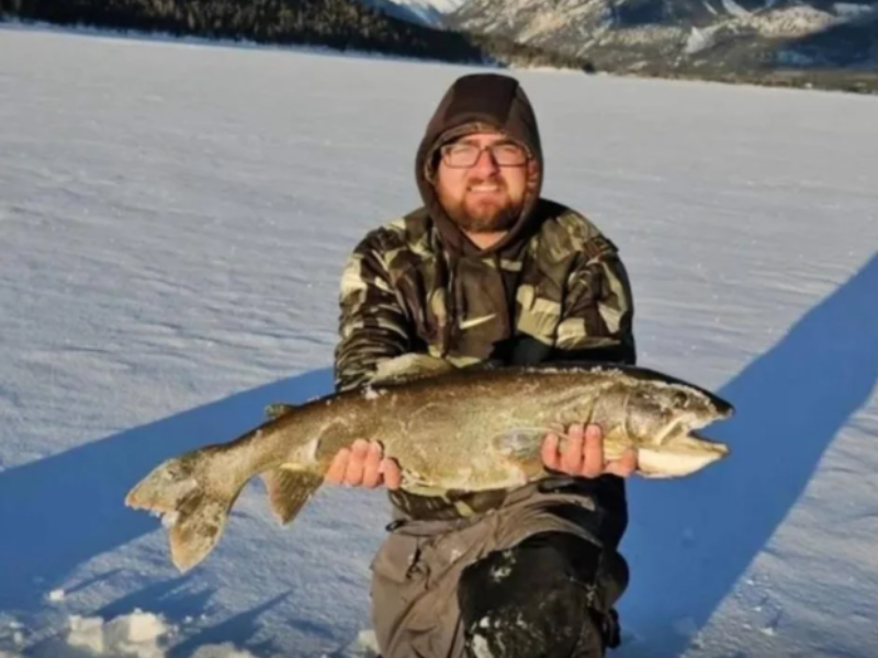 Man kneels down holding a large fish on an icy lake