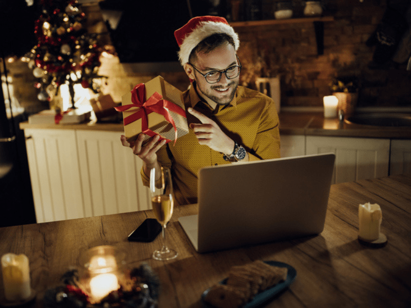 Man holding Christmas present while chatting on laptop