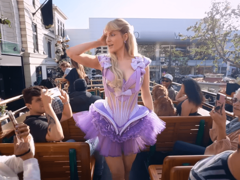 Meghan Trainor wearing a purple dress on an open top tour bus