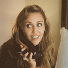 Miley Cyrus holding a a black shoe to her ear like a phone