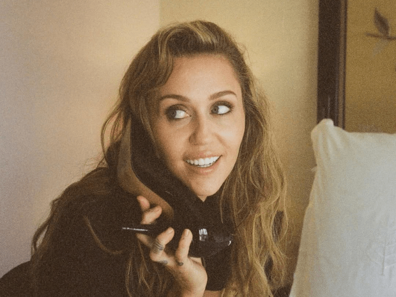 Miley Cyrus holding a a black shoe to her ear like a phone