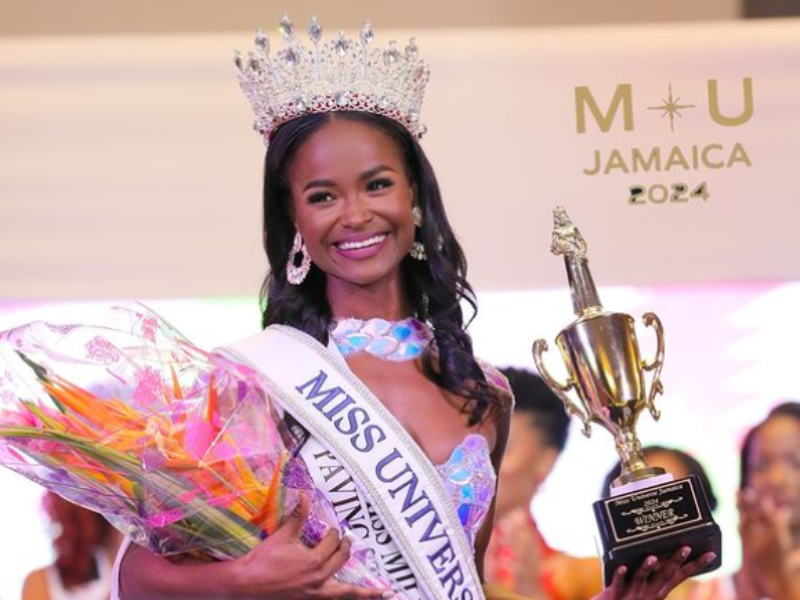Miss Universe Jamaica poses on stage with her crown and flowers