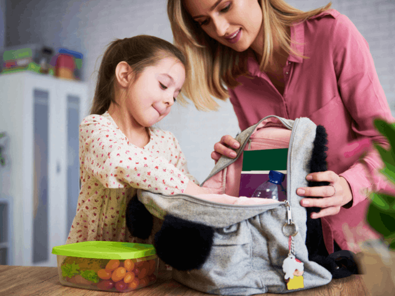 Mom and daughter packing school lunch in a backpack