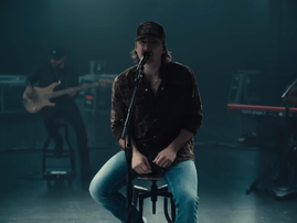 Morgan Wallen sitting on a stool while performing