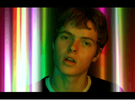 Moses Martin poses against a background with colourful vertical streaks