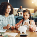 Mother and daughter sit at a kitchen table with a piggybank