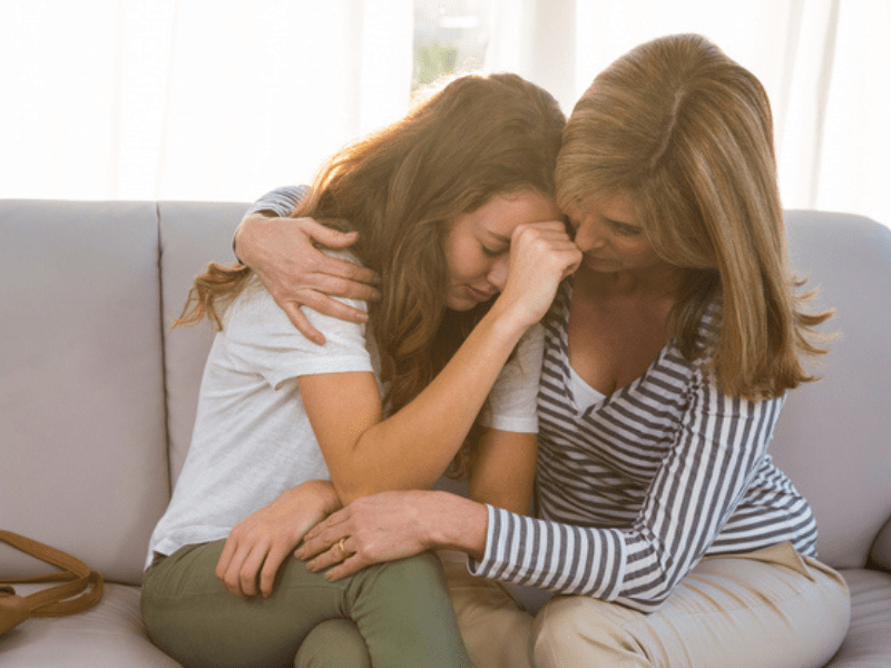 Mother consoles sad daughter on a grey couch