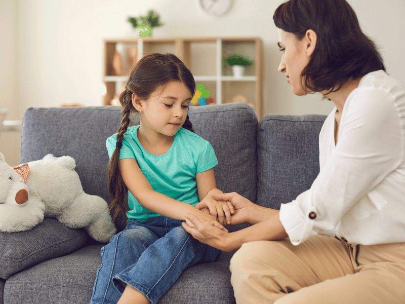 Mother sitting with daughter, holding her hands, talking to her and teaching her something