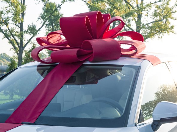 New white car with red gift ribbon and bow awaits its buyer in the cabin