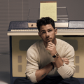 Nick Jonas posing against an upright piano