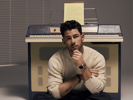 Nick Jonas posing against an upright piano
