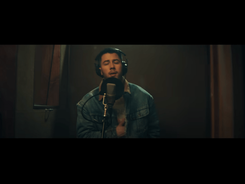 Nick Jonas wears headphones while singing into a mic